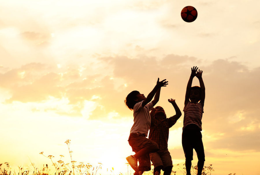Group Of Happy Children Playing With Ball On Meadow Sunset Summertime